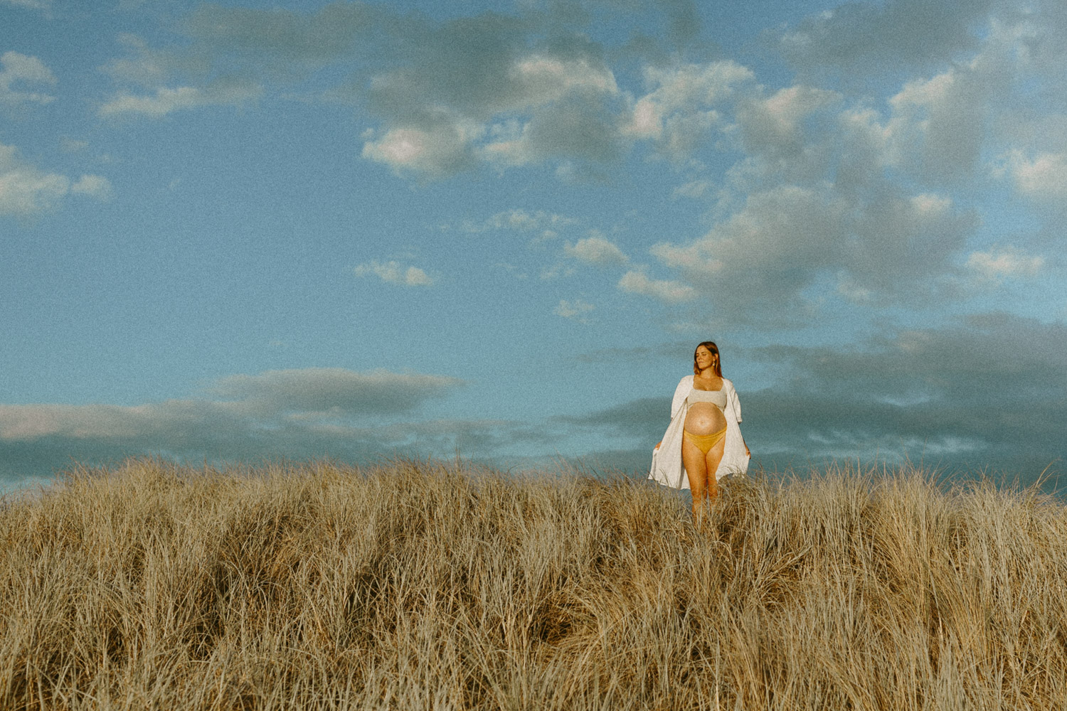pregnant lady standing on grassy hill at beach in harsh sunlight