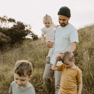 Dad in beanie with three kids walking down grass hill in earthy tones
