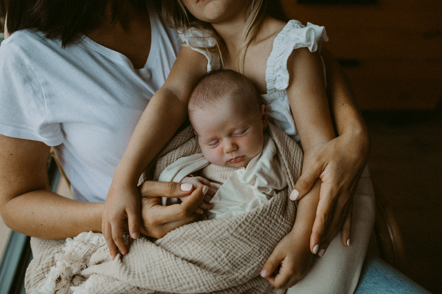 baby cuddled by mum and sister in natural coloured blanket