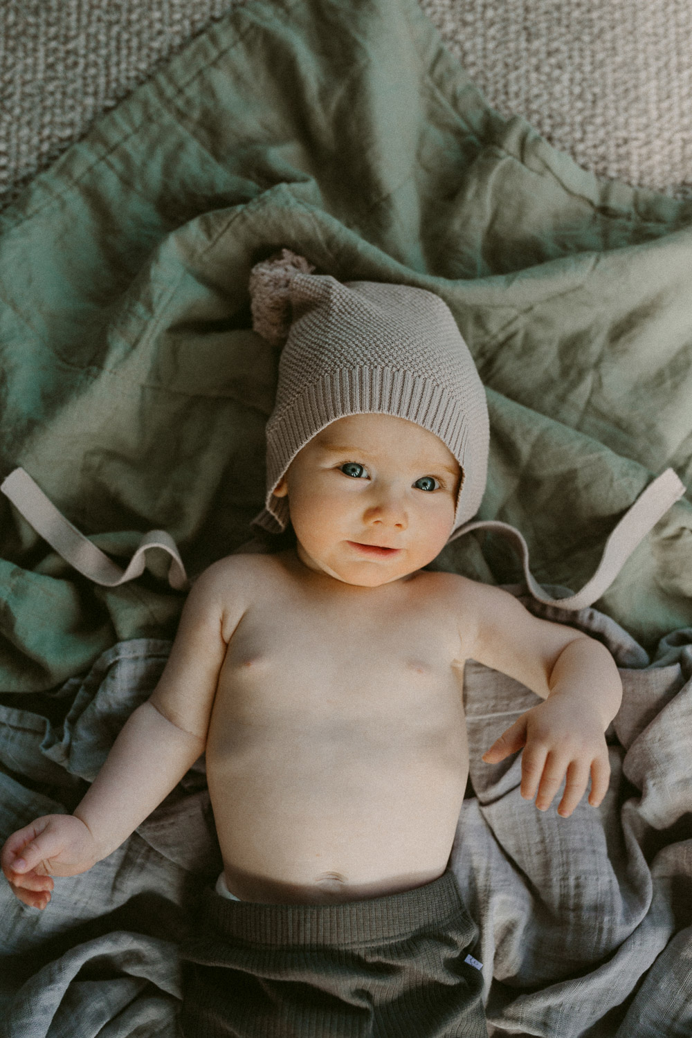 baby in cute knitted beanie lying on muted green blanket