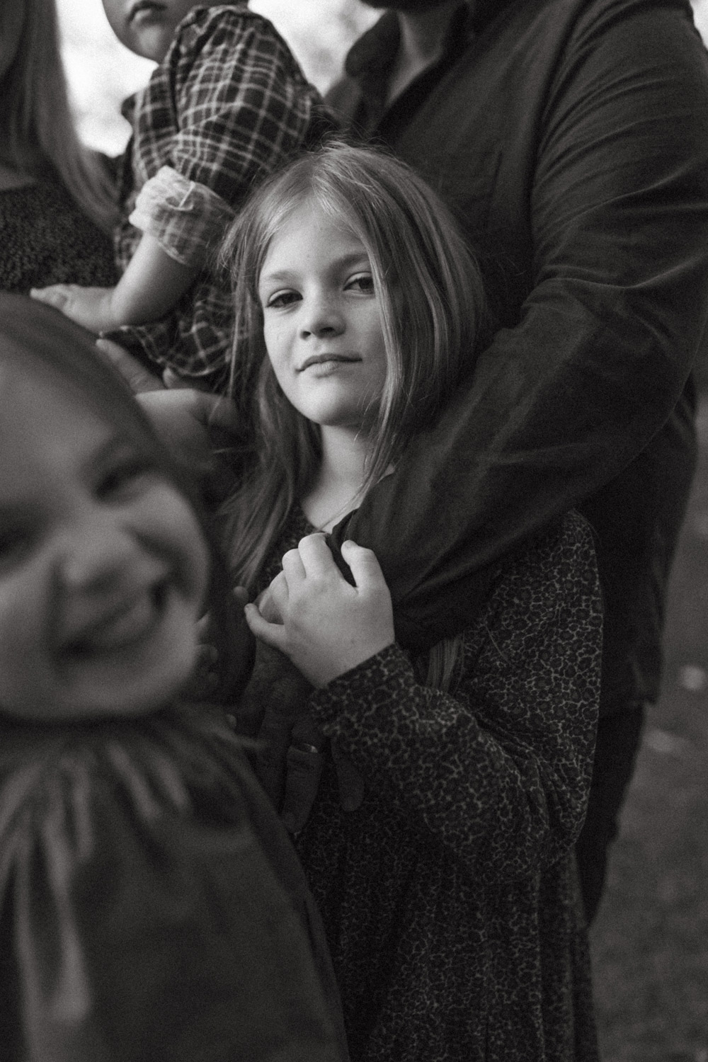 portrait of girl holding her dads arm with family close by