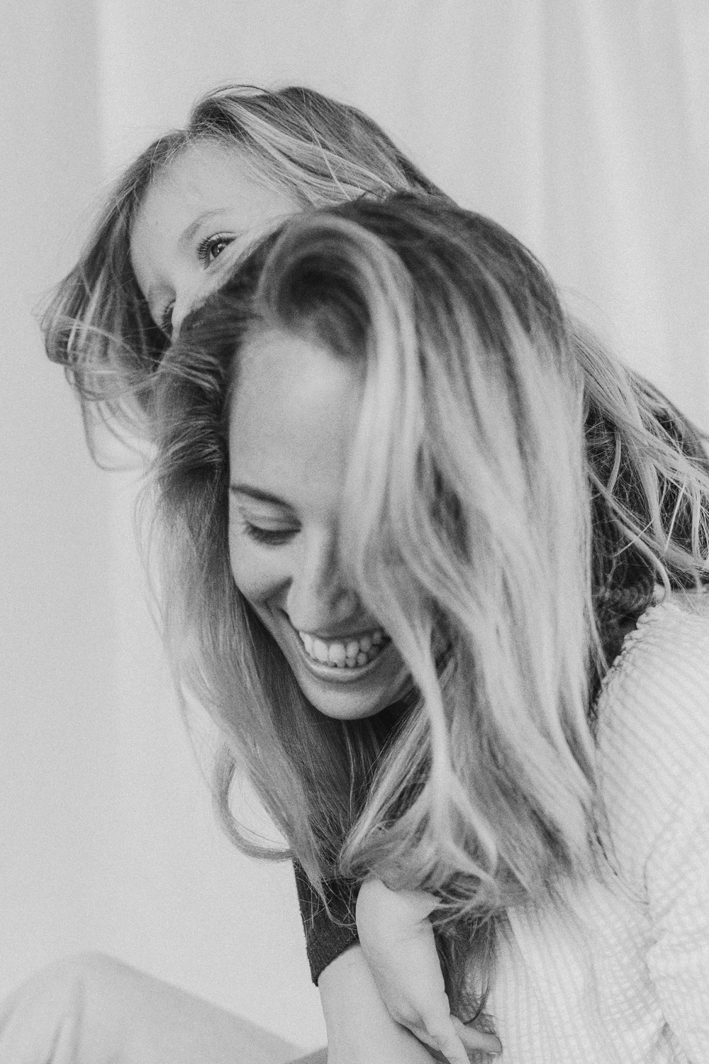 Little girl jumping on her mums back, big smiles against a white linen backdrop