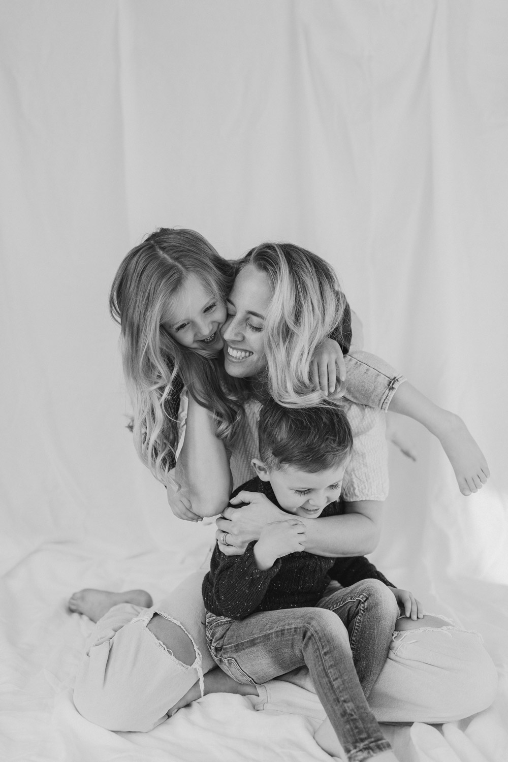 Mum with her little kids, big smiles against a white linen backdrop