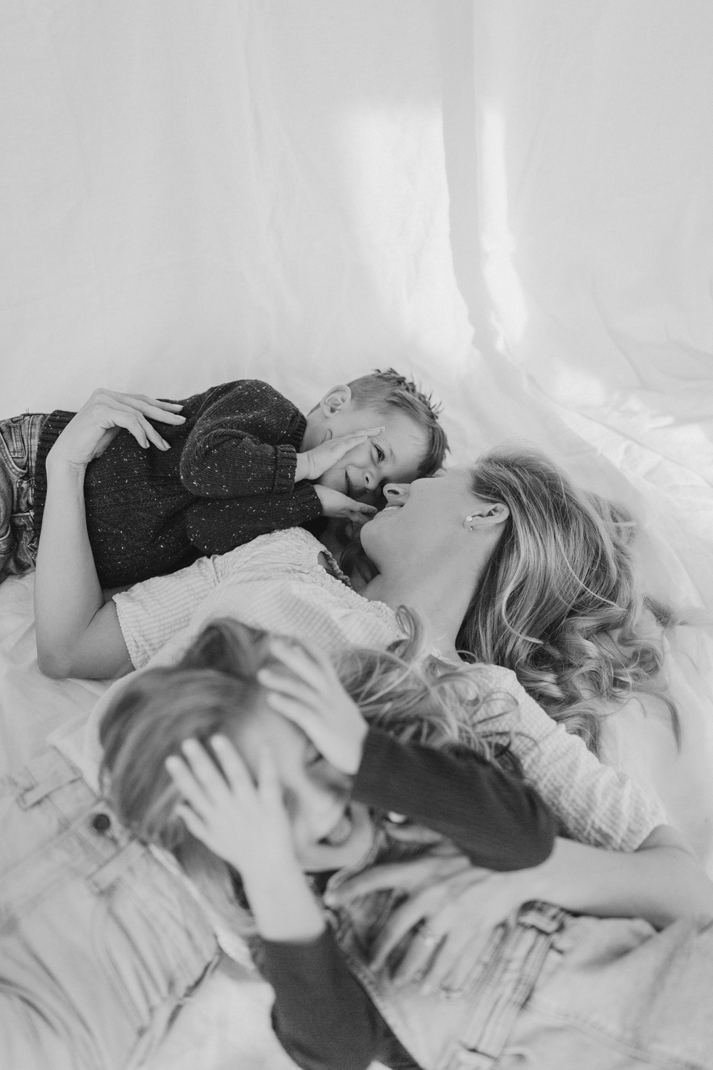 Mum lying down with her little kids against a white linen backdrop