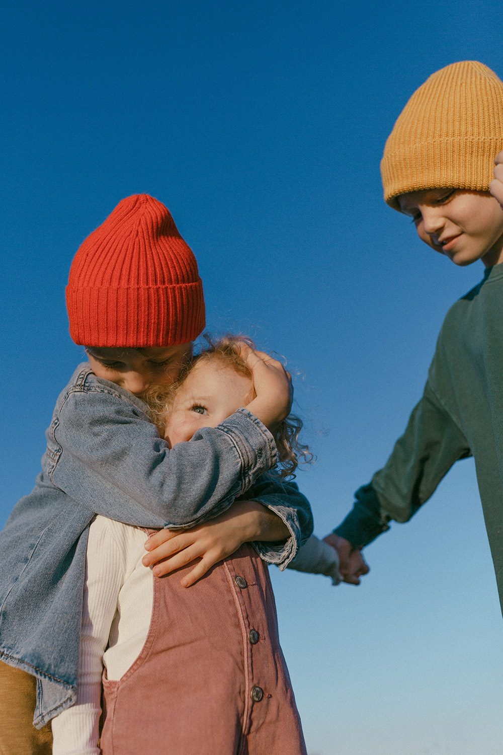 3 young siblings wearing bright colours outside in the sun