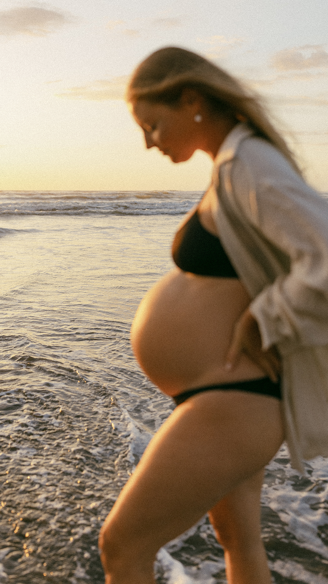 Pregnant lady feet in water at beach with sunset